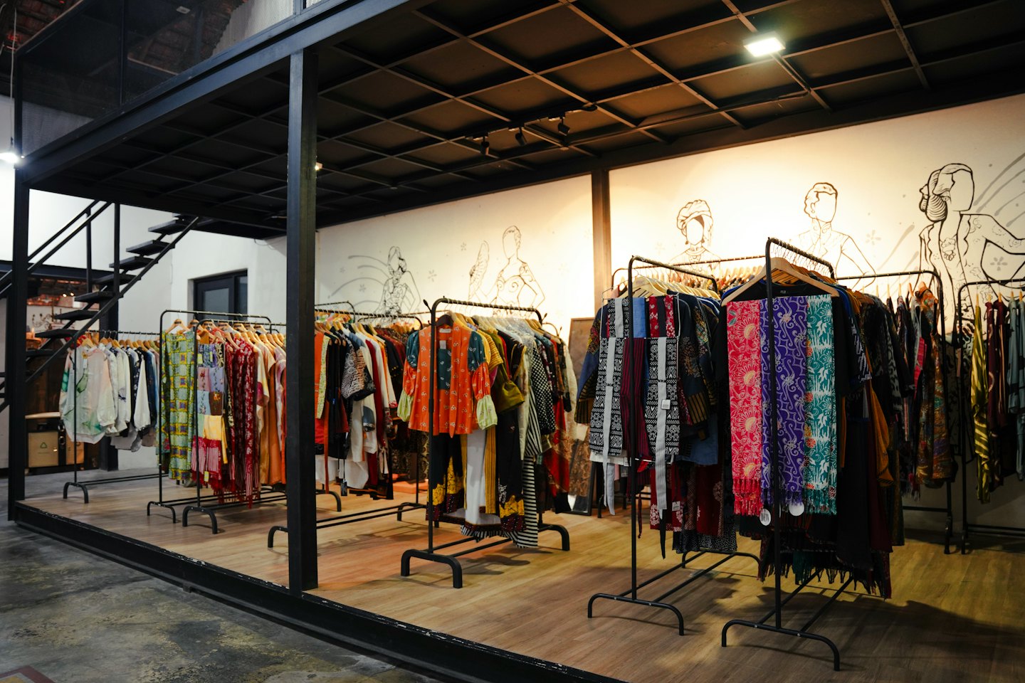 Butik odzieżowy z kolorowymi wzorzystymi ubraniami na wieszakach i industrialnymi ramami.