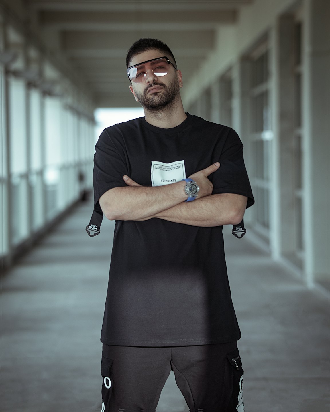 Mężczyzna w streetwearze i okularach przeciwsłonecznych z różowymi szkłami stojący na korytarzu.